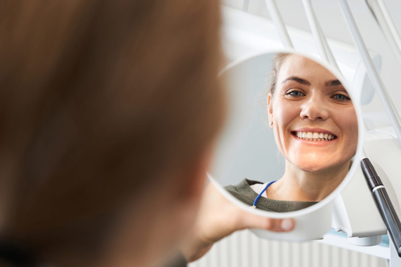 Attractive caucasian lady checking her beautiful smile in mirror after stomatological treatment.