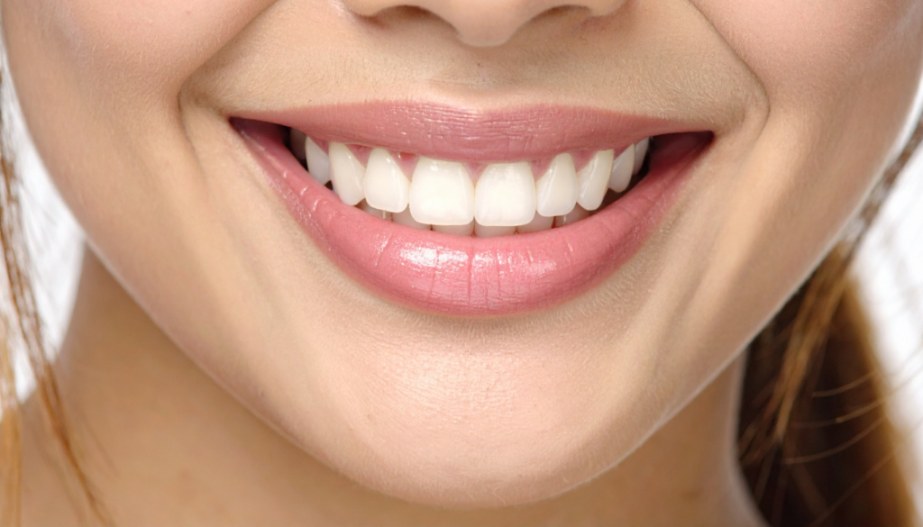 Close-up of a smiling mouth showing white, straight teeth and pink lips.