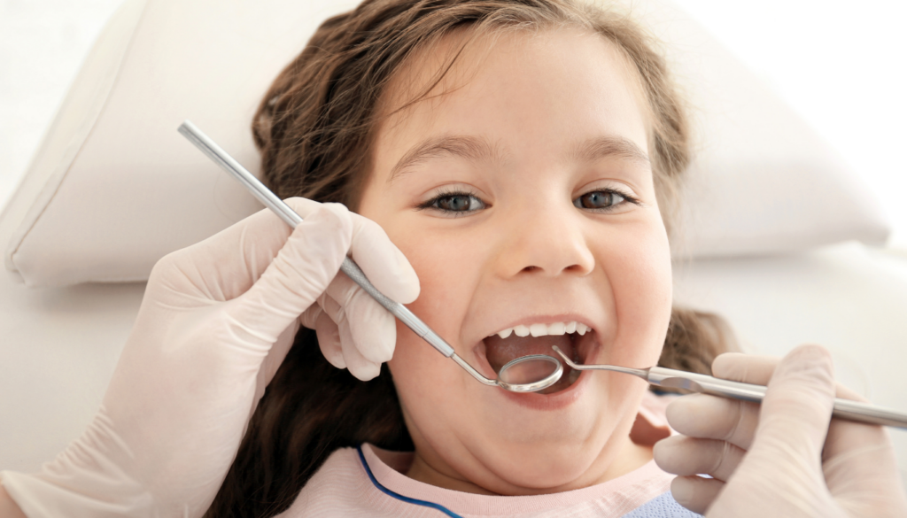 Young girl at the dentist with mouth open as dental tools inspect her teeth (gloved hands visible).
