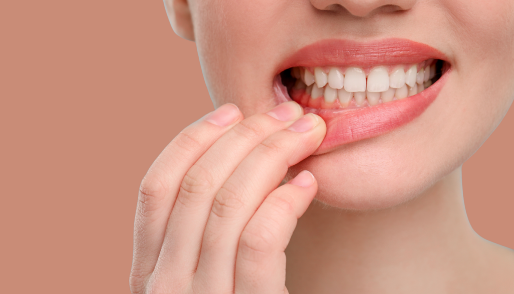 dana-st-dental-gum-health | Dana Street Dental Close-up of a person biting their lower lip with fingers, pink lipstick, peach background.