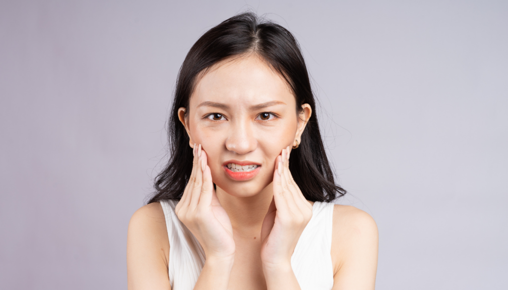 Woman presses her cheeks with both hands, grimacing in facial pain or discomfort.